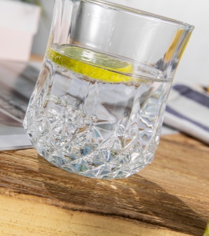 Close-up angled shot of a commercial-grade restaurant glass cup with diamond cut pattern, filled with iced water and a lemon slice on a wooden table.