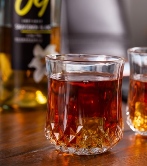Faceted base crystal whiskey glass tumbler filled with dark amber liquor, sitting on a wooden table next to a branded bottle, perfect for custom logo engraving.