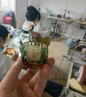 Carved whiskey glass The image shows a glass with an engraved pattern on its surface, with a workshop where glass surface processing is done in the background.