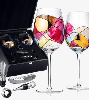 This image, taken against a clean, pure white background, showcases a high-end hand-painted art wine glass and accessory gift set, part of a gifting and promotional program. On the right side of the image stand two tall crystal wine glasses, their surfaces adorned with vibrant, hand-painted Art Deco style artwork: flowing black lines divide the glass into irregular geometric blocks filled with highly transparent gold, deep rose, bright yellow, light blue, and orange-red, refracting long, microcrystalline highlights under white sunlight. To the left and behind is an open, rectangular, high-end black wooden or hard leather gift box. The lid is lined with dark black premium flocked material, and the complete metal wine set is neatly stored in the foam recesses inside. On the pure white mirrored floor in front of the gift box, four matching wine accessories made of metal and rubber are meticulously displayed: from top to bottom, a silver stainless steel multi-functional corkscrew with serrations and a screwdriver; a pointed, inverted conical wine stopper with a silver metal ball handle and a black rubber ring; a metal wine dispenser with a spout; and a black wine dispenser base or paper cutter. The entire image is compact in composition and clear in product details, perfectly showcasing the artistic luxury of high-end custom hand-painted glassware and the professional style of a one-stop commercial gift supply chain.