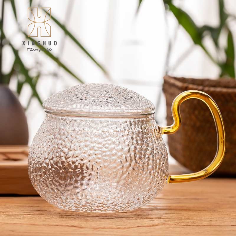 Image of hammered glass teacups with gold handles displayed on a wooden tea table.